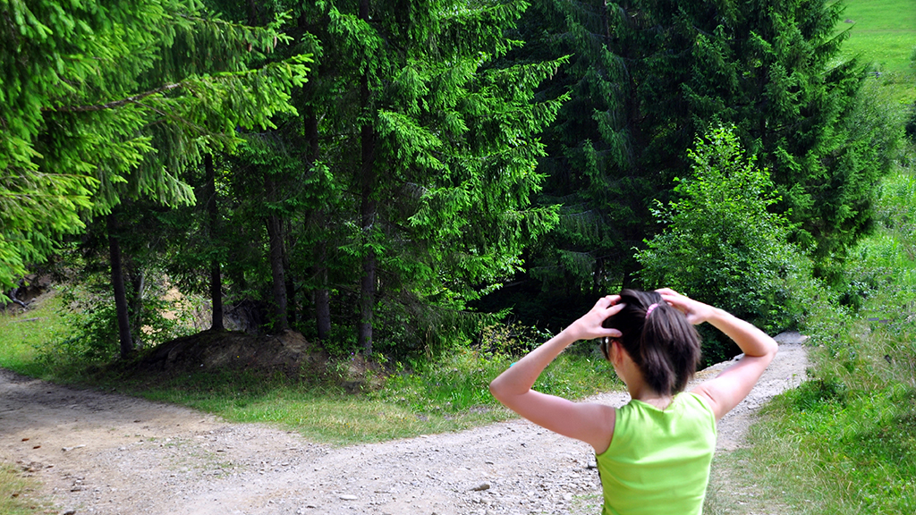 Jugendliche steht an einer Wegkreuzung und hält die Hände an den Kopf