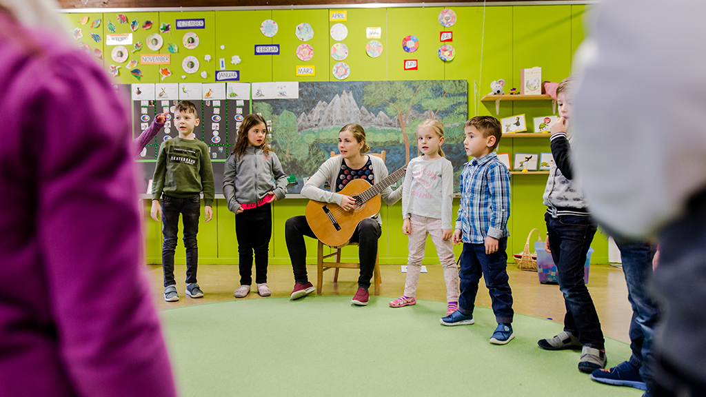 Lehrperson spielt Gitarre und die Lernenden singen dazu