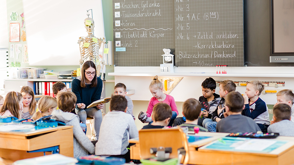 Lehrperson sitzt mit Klasse im Kreis und liest vor