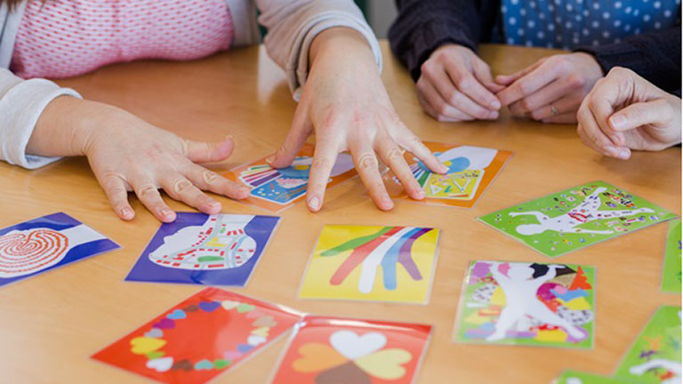 Verschiedene Hände zeigen auf Bilder welche auf einem Tisch liegen