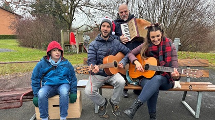 Drei Lehrpersonen und ein Schüler mit Instrumenten - im Freien auf einer Bank sitzend und musizierend