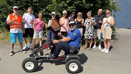 Polizist sitzt auf einem Go-Kart anlässlich der Verabschiedung, im Hintergrund verschiedene Lehrpersonen